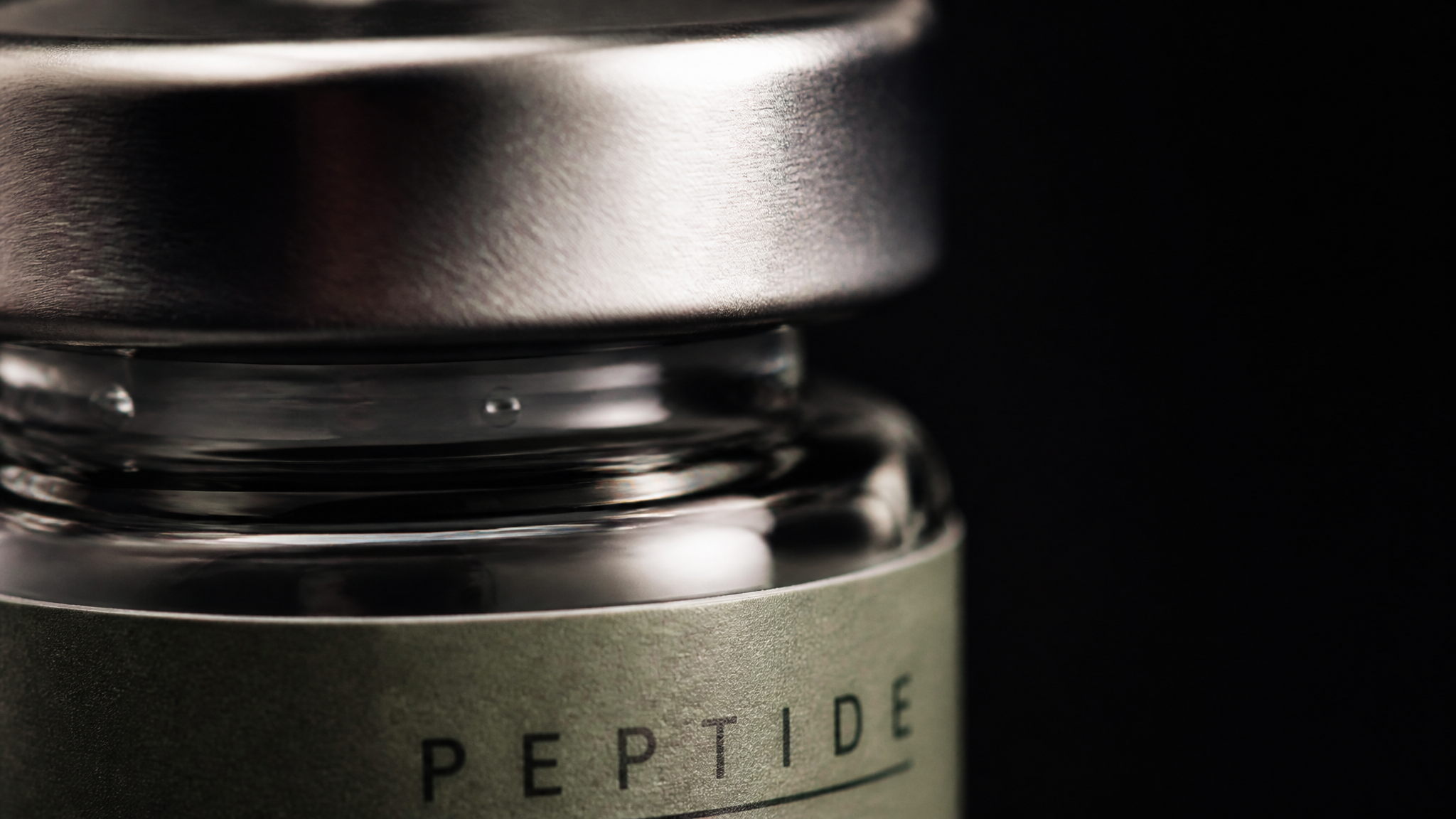 Extreme macro detail of a brushed-silver vial cap and sage-labeled peptide vial